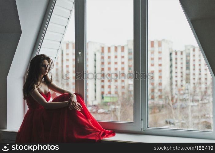 Beautiful girl in dress sits by the window.. Girl in evening gown sits on a windowsill 5981.