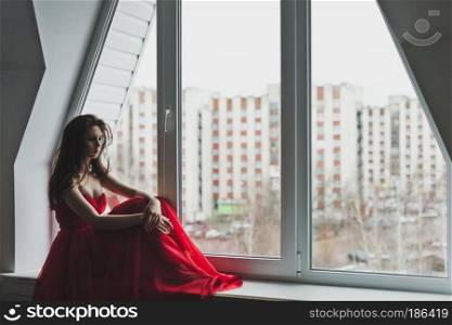 Beautiful girl in dress sits by the window.. Girl in evening gown sits on a windowsill 5981.