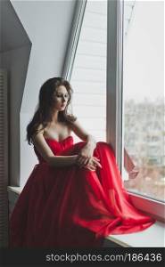 Beautiful girl in dress sits by the window.. Girl in evening gown sits on a windowsill 5982.