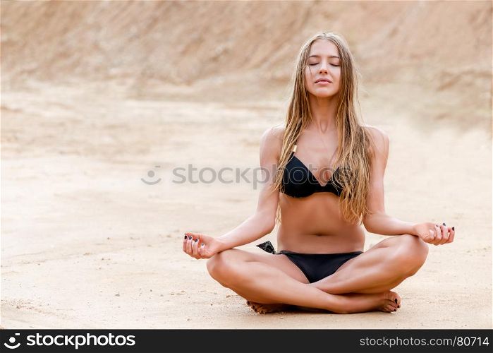 beautiful girl in lotus pose relaxes on sand in bikini