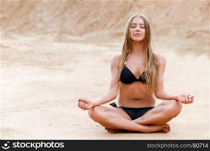 beautiful girl in lotus pose relaxes on sand in bikini
