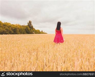 Beautiful girl in red retro dress standing in golden field. Freedom concept. Happy woman outdoors. Harvest, agriculture concept.