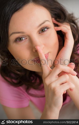 Beautiful girl in the bedroom looking at camera and showing silence gesture