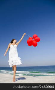 Beautiful girl jumping with red ballons in the beach