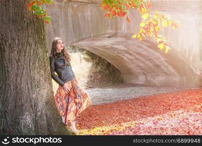 Beautiful girl leaning against a big tree with colorful leaves, looking up, enjoying the autumn atmosphere, in Schwabisch Hall, Germany.