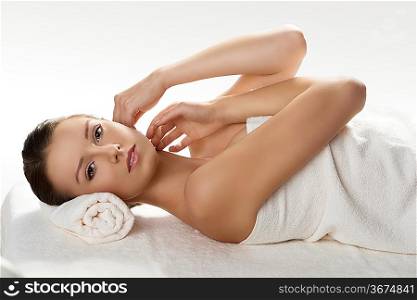 beautiful girl lying on a table with withe towel on her body and under her head, she looks in to the lens and has both hands near the face