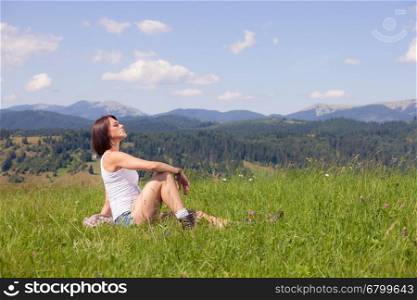 Beautiful girl lying on green grass field and holding flower in her mouth