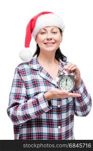 Beautiful girl meets New Year in pajamas with an alarm clock in . Beautiful girl meets New Year in pajamas with an alarm clock in her hands, a red cap on her head
