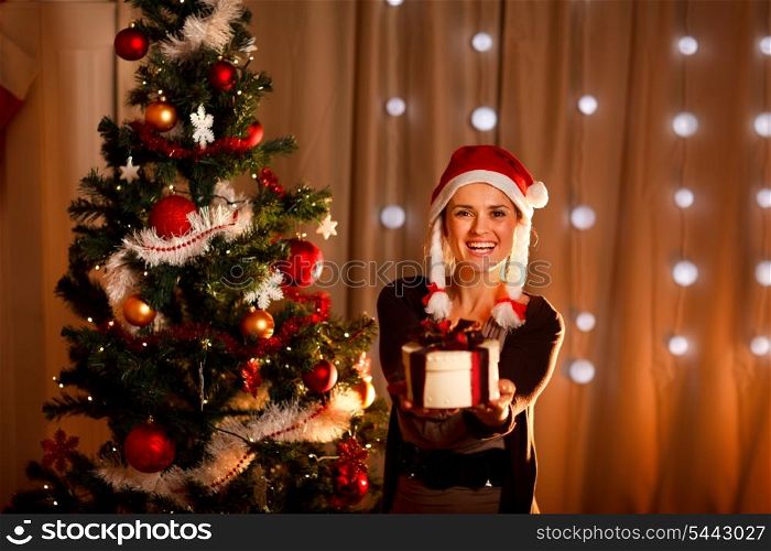 Beautiful girl near Christmas tree presenting gift box&#xA;