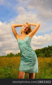 Beautiful girl on the field and blue cloudy sky behind her