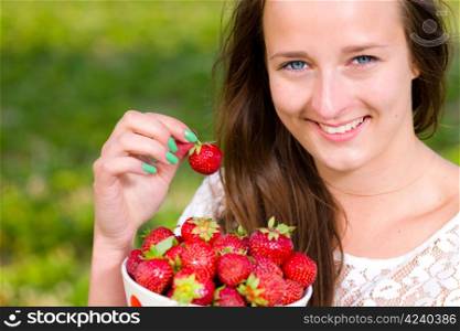 Beautiful girl pick up a strawberry from a bowl, focus on the eyes