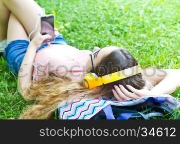 Beautiful girl relaxing and listen music in the headphones in the park