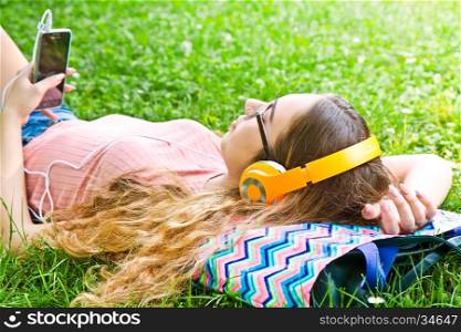 Beautiful girl relaxing and listen music in the headphones in the park
