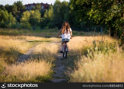 Beautiful girl riding bike at fields at sunset