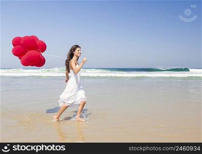 Beautiful girl running in the beach with red ballons in her hand