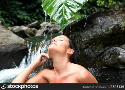 Beautiful girl showering in river under waterfall