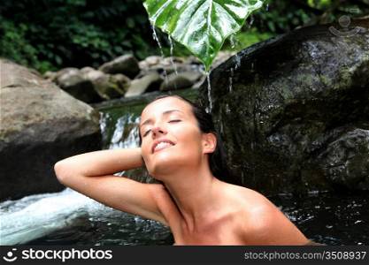 Beautiful girl showering in river under waterfall