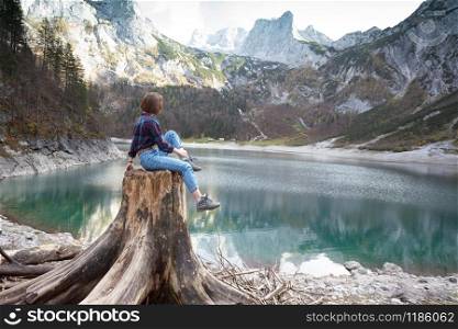 beautiful girl sits on a stump on a background of a mountain lake