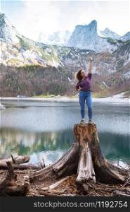 beautiful girl sits on a stump on a background of a mountain lake