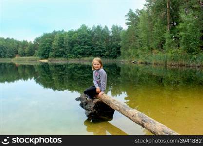 beautiful girl sits on the log by the river. little beautiful girl sits on the log by the river