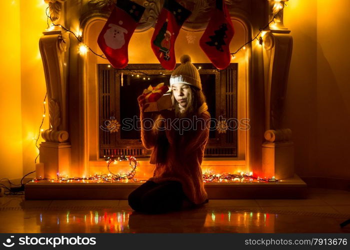 Beautiful girl sitting at dark living room at Christmas and looking inside gift box