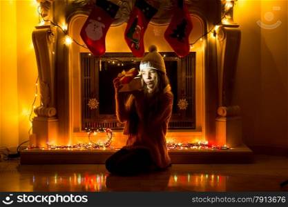 Beautiful girl sitting at dark living room at Christmas and looking inside gift box
