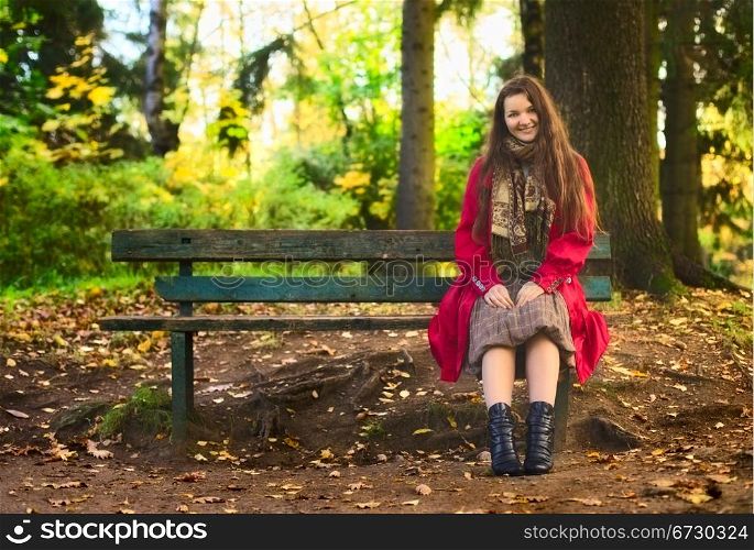 beautiful girl sitting on bench in enchanted autumn park