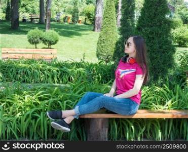 beautiful girl sitting on bench in green park, sunny day. the girl of Asian appearance. young girl in a picturesque park