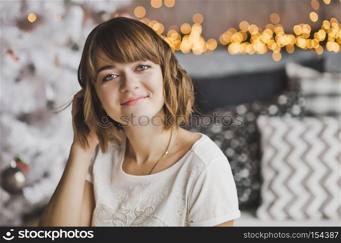 Beautiful girl sitting on the carpet near the Christmas tree.. Portrait of a girl with a pretty face in the Christmas lights 7210.