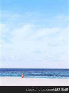 Beautiful girl sitting on white sandy beach, enjoying warm sunny day, taking sunbath, copy space, summer holidays and vacation concept