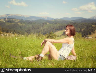 Beautiful girl smiling and lying on field of green grass and holding flowers in her mouth