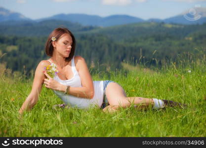 Beautiful girl smiling and lying on field of green grass and holding flowers in her hand