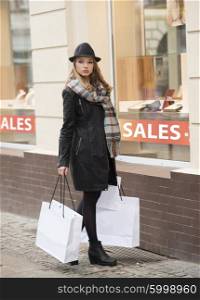 beautiful girl standing near a wiandow shop , she is looking in camera like a sophisticated lady , she has shopping bags