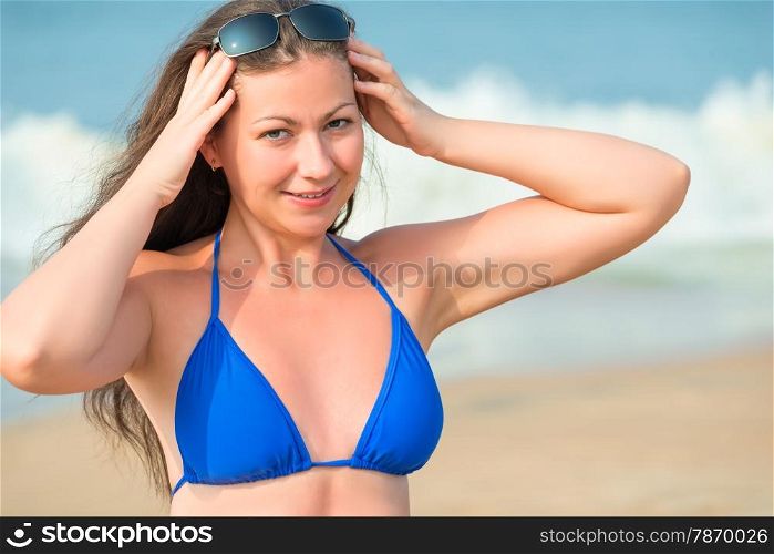 beautiful girl straightens sunglasses on background of sea waves