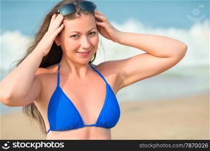 beautiful girl straightens sunglasses on background of sea waves