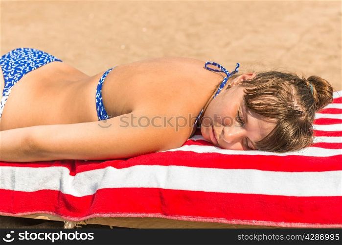 beautiful girl sunbathes on a beach in a lounge chair
