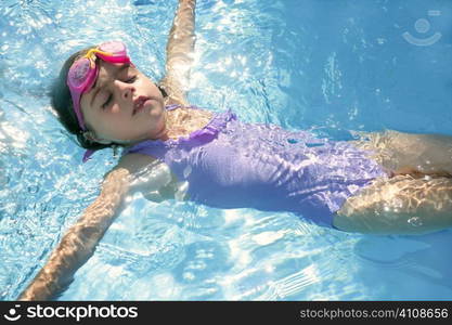 Beautiful girl swimming on blue pool with pink goggles