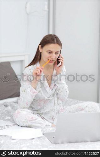 beautiful Girl talking on the phone in home. Woman working, learns and using laptop computer in the bedroom. Freelancer. Writing, typing. Communication and technology concept. beautiful Girl talking on the phone in home. Woman working, learns and using laptop computer in the bedroom. Freelancer. Writing, typing. Communication and technology concept.