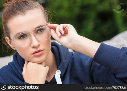 Beautiful girl teenager female young woman with blue eyes outside wearing dark blue hoodie and glasses