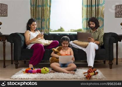 Beautiful girl using tablet on carpet while her parents busy with smartphone and laptop on sofa