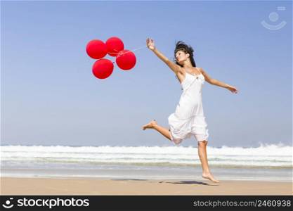 Beautiful girl walking in the beach and holding red balloons