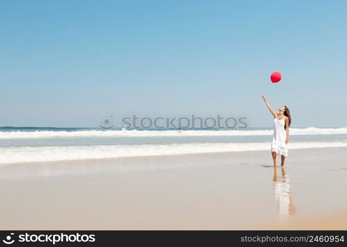 Beautiful girl walking in the beach with red ballons in her hand