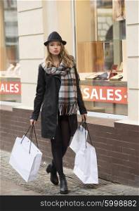 beautiful girl walking near a window shop , in the street . she is doing shopping in winter sale , dressing a coat and hat