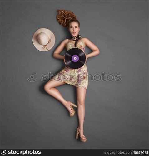 Beautiful girl, wearing vintage music headphones around his neck and holding a purple LP microgroove vinyl record on chalkboard background.