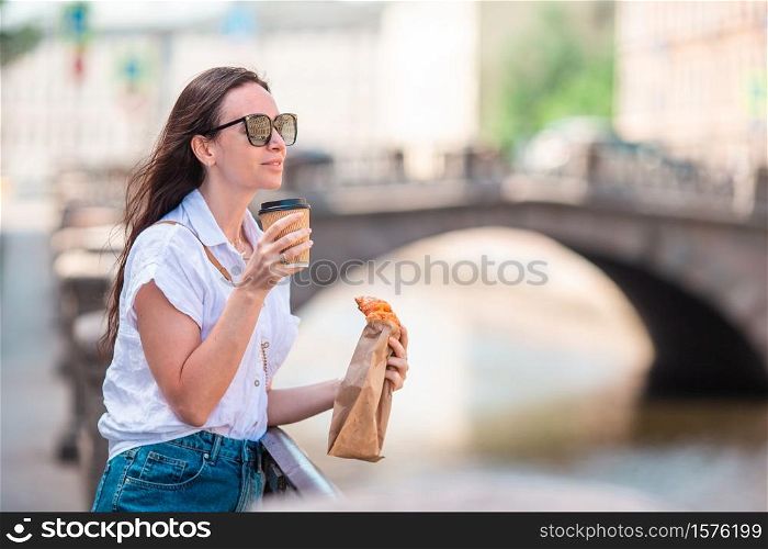 Beautiful girl with a croissant and coffee outdoors on the promenade in Saint Petersburg. Woman with a croissant and coffee outdoors on the promenade
