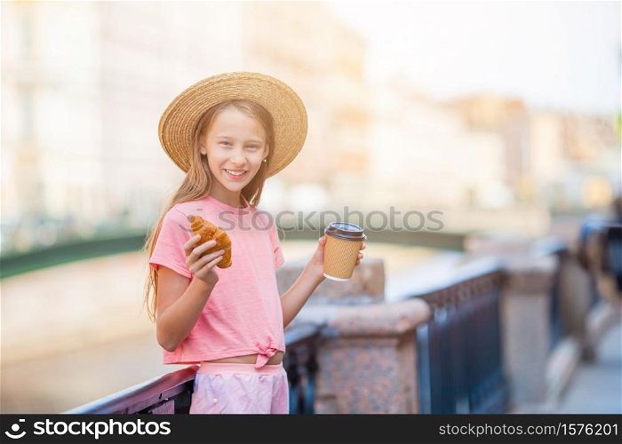 Beautiful girl with a croissant and coffee outdoors on the promenade in Saint Petersburg. Woman with a croissant and coffee outdoors on the promenade