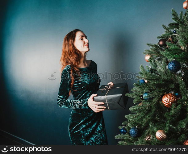 Beautiful girl with a gift box near Christmas tree, smiling. New Year and Christmas concept. Home and family warmth. Copy space for your text and design