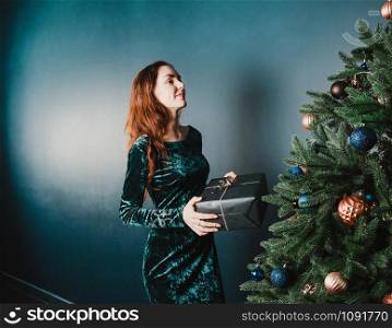 Beautiful girl with a gift box near Christmas tree, smiling. New Year and Christmas concept. Home and family warmth. Copy space for your text and design