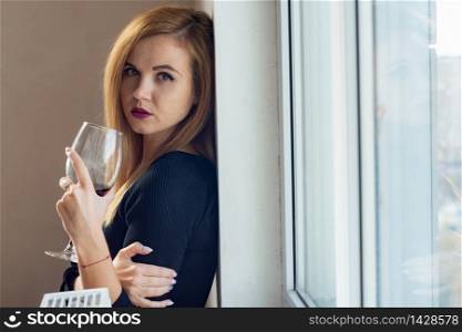 Beautiful girl with a glass of wine in her hands stands at the window
