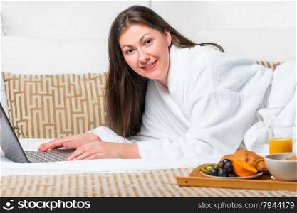 beautiful girl with a laptop in bathrobe on the bed